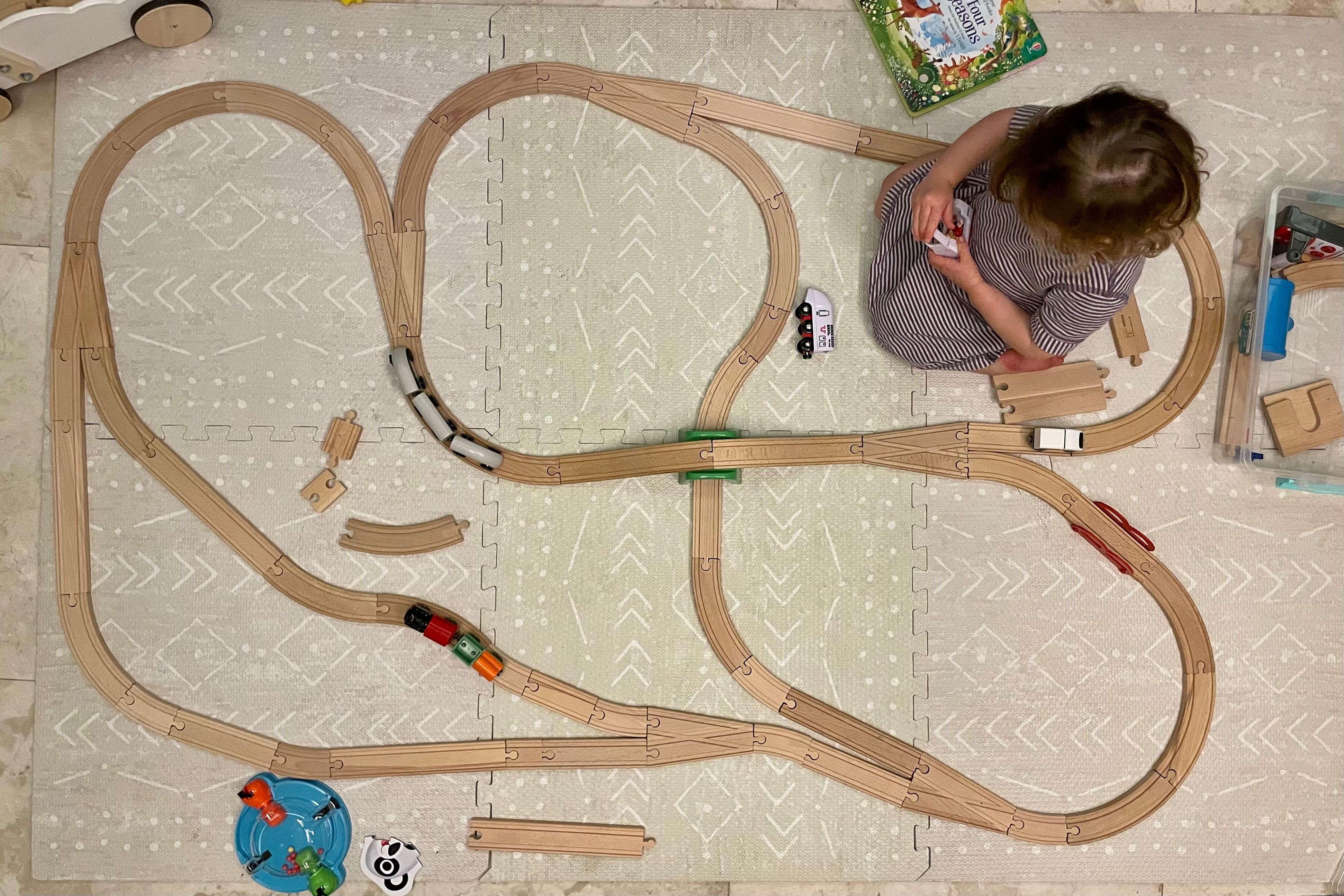 Bird’s-eye-view of a track layout including 6 forks and an overpass, with Verity sitting in the middle, looking down at a train in her hands.